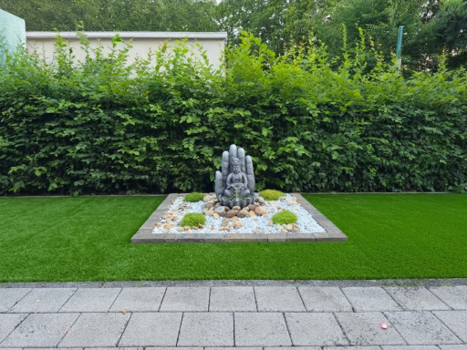 Buddha-Statue eingebettet in ein stilvolles Steinbeet auf einer gepflegten Rasenfläche.